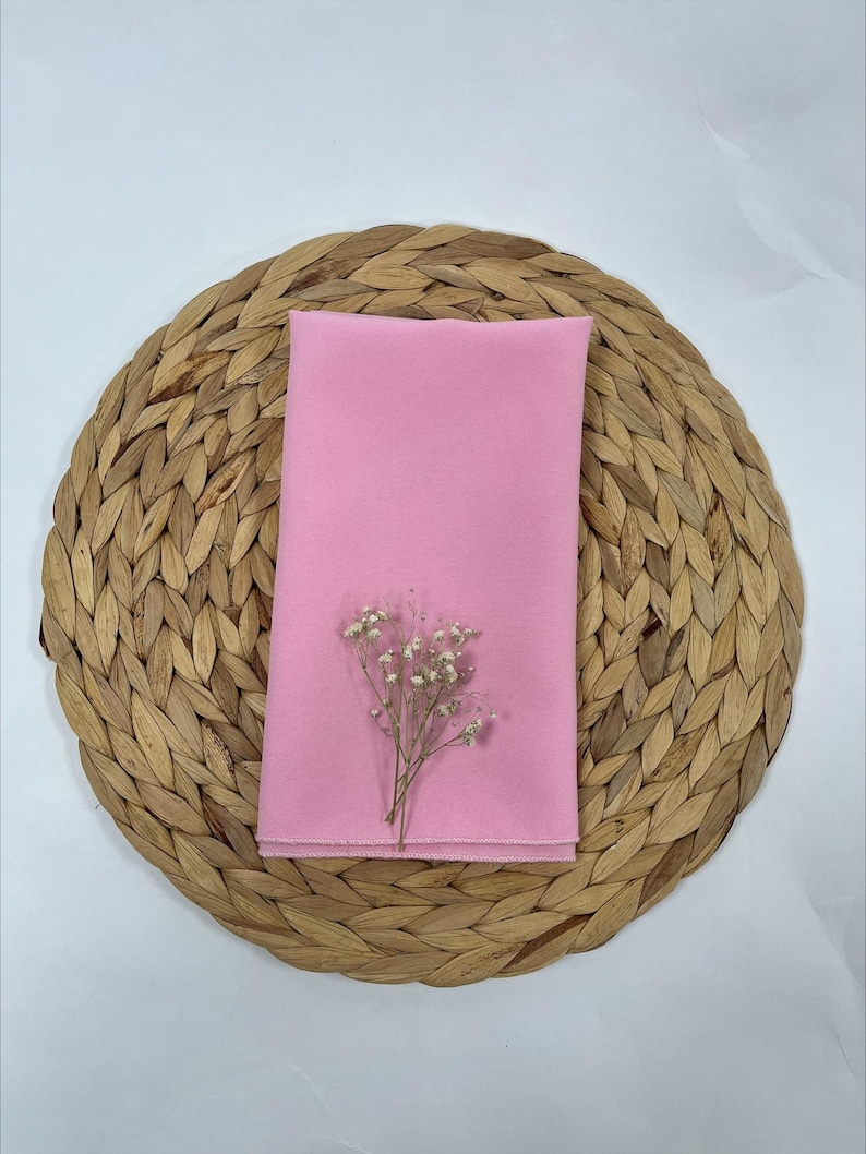 May include: A pink fabric napkin on a woven round placemat with a small bouquet of white flowers.