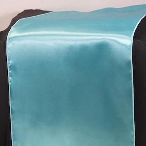 Puede incluir: Un camino de mesa de satén turquesa. El camino de mesa es liso y tiene un brillo sutil.