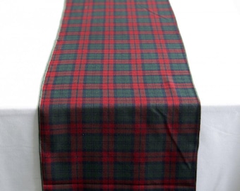 May include: A rectangular table runner featuring a classic plaid pattern with intersecting lines in deep forest green, navy blue, and vibrant red. The fabric has a woven texture and is laid out vertically, displaying a consistent grid design throughout.
