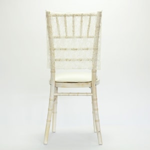 May include: A white wooden chair with a cream-colored cushion and a lace chair cover. The chair has a bamboo-style frame and is set against a white background. The lace cover adds a touch of elegance.