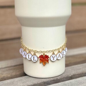 May include: A gold chain bracelet with white enamel charms spelling out "FALL Y'ALL" and a red and orange enamel maple leaf charm.