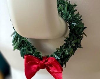 May include: A green Christmas wreath with a red bow. The wreath is made of green paper and is about 10 inches in diameter.