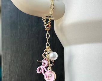 May include: A gold chain charm with a pink enamel letter "P" charm, a pink bow charm, and a white pearl charm.