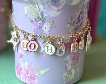 May include: A gold chain charm bracelet with pink, white, and green enamel charms that spell out "HO HO". The charms are attached to a gold chain with a lobster clasp.