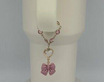 May include: A delicate gold chain necklace with pink crystal accents. The necklace features a heart-shaped pendant with a clear crystal center and a pink bow charm.