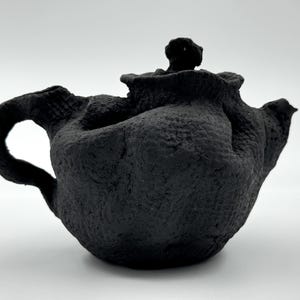 May include: A black ceramic teapot with a textured surface and a rounded body. The teapot has a small spout and a lid with a knob.