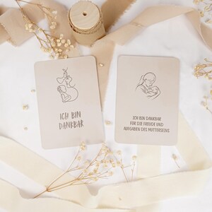 May include: Two rectangular beige cards featuring black line art illustrations of a parent holding a baby. The left card displays the text ICH BIN DANKBAR. The right card displays the text ICH BIN DANKBAR F&Uuml;R DIE FREUDE UND AUFGABEN DES MUTTERSEINS.