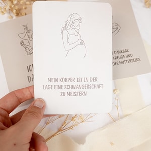 May include: A rectangular white card featuring a minimalist black line drawing of a pregnant person holding their belly. Below the illustration, the German text reads: MEIN K&Ouml;RPER IST IN DER LAGE EINE SCHWANGERSCHAFT ZU MEISTERN in a simple sans-serif font.