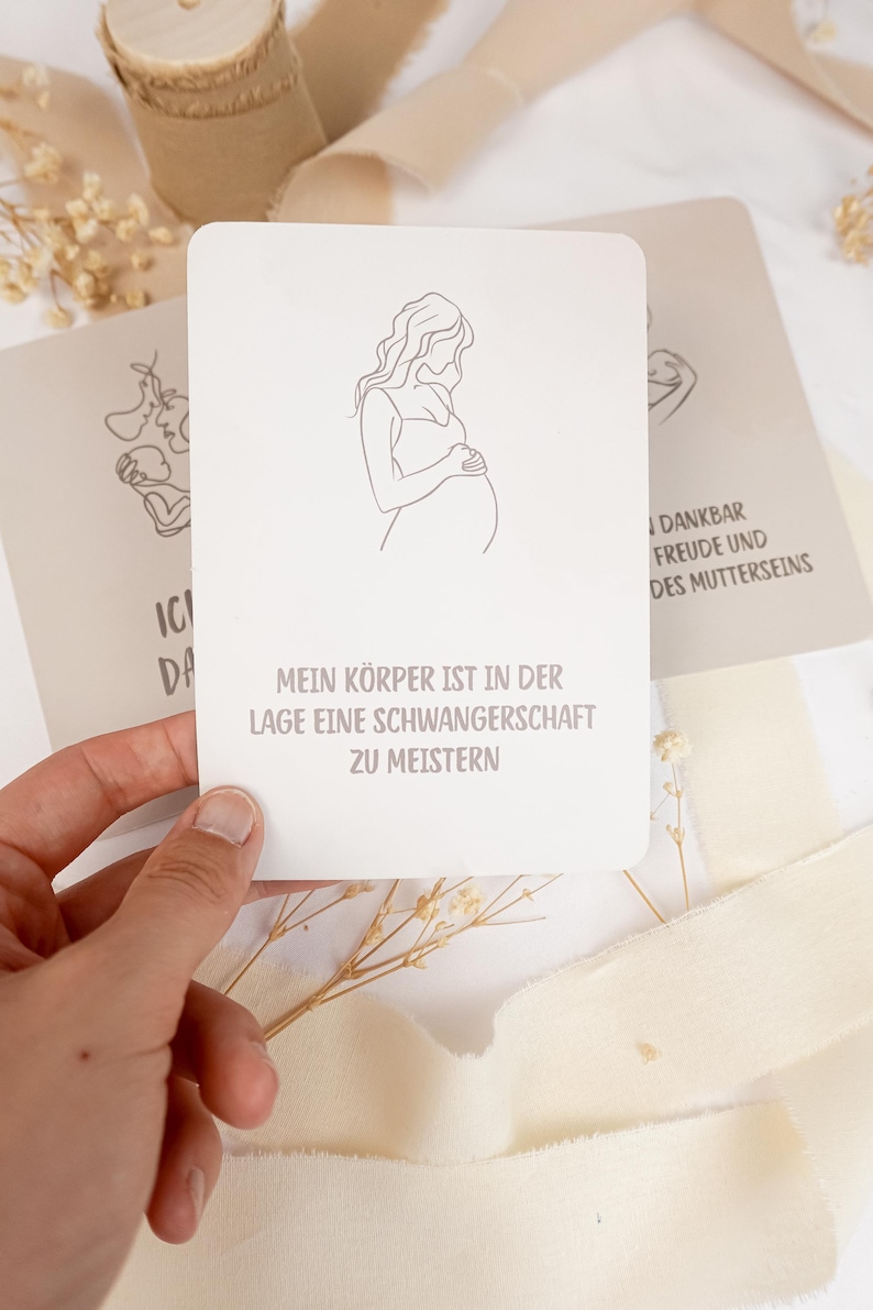 May include: A rectangular white card featuring a minimalist black line drawing of a pregnant person holding their belly. Below the illustration, the German text reads: MEIN K&Ouml;RPER IST IN DER LAGE EINE SCHWANGERSCHAFT ZU MEISTERN in a simple sans-serif font.