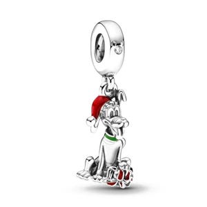 May include: A silver charm depicting a cartoon dog wearing a red Santa hat and a green collar. The dog is holding a red and white gift. The charm has a loop with a small clear stone.