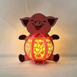 May include: A pink pig holding a red paper lantern with a yellow heart pattern. The lantern is lit from inside, creating a warm glow.