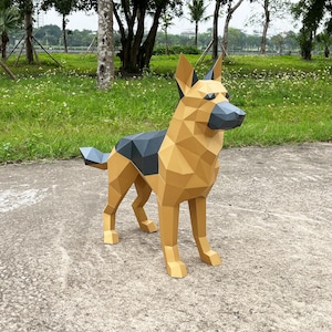 May include: A papercraft model of a German Shepherd dog. The dog is standing on a concrete surface with green grass in the background. The dog is made of brown and black paper and has a realistic appearance.