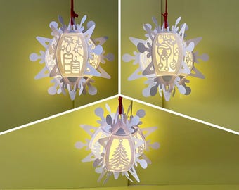 May include: Three white paper snowflake ornaments with cut-out designs, illuminated from within, hanging from red strings. The designs include a Christmas tree, candles, and a bell.