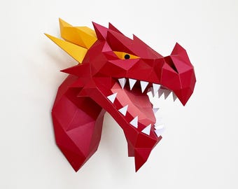 May include: A red papercraft dragon head with yellow horns and sharp white teeth. The dragon's mouth is open, revealing a pink interior. The artwork is mounted on a white wall, showcasing a geometric, polygonal design.