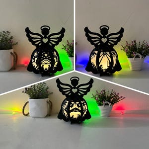 Könnte beinhalten: Schwarze Metallengel-Silhouette mit einem Ausschnitt der Weihnachtsgeschichte. Der Engel hält ein Herz in seinen Händen. Der Engel wird mit einem warmen weißen Licht beleuchtet.