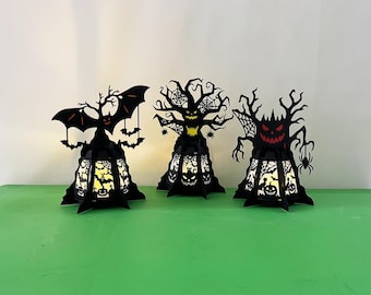May include: Three black Halloween tree lanterns with cut-out designs. One lantern features a bat, another has spiderwebs, and the third has a red-eyed face. Each lantern has a light inside, creating a spooky glow.