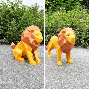 May include: Two geometric paper lion sculptures. One is seated, the other standing. Both are primarily yellow with brown manes and tails. The sculptures are on a gray surface with green foliage in the background.