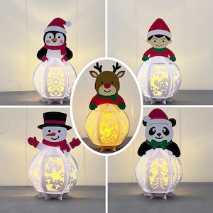 May include: A collection of five Christmas-themed paper lanterns. Each lantern has a white, spherical design with cut-out patterns and is topped with a different festive character, including a penguin, snowman, panda, reindeer, and elf.
