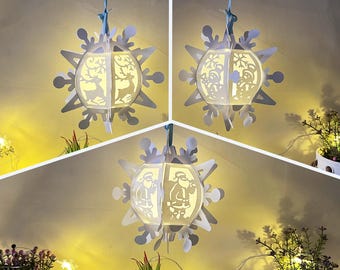 May include: Three white paper snowflake lanterns with LED lights. The lanterns are decorated with Christmas-themed designs, including Santa Claus, reindeer, and snowflakes.