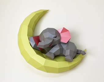 May include: A gray geometric elephant with pink ears and red accents rests on a light green crescent moon. The papercraft animal is a whimsical decorative item, perfect for a nursery or children's room.