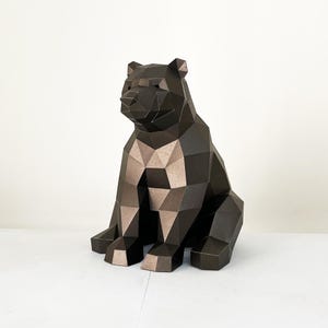 May include: A geometric, dark brown bear sculpture in a sitting position. The bear's body is constructed from multiple triangular and quadrilateral shapes, creating a faceted appearance. The bear's chest and paws have a lighter brown color. The background is plain white.