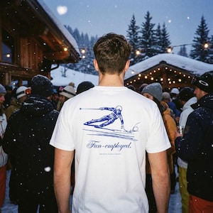May include: White t-shirt with a blue graphic of a skier in action. The shirt also features the text "Fun-employed" in a cursive font, with "aesthetic athletic people" below. The design is on the back of the shirt.