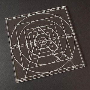 May include: A clear, rectangular drafting tool featuring white geometric patterns, such as squares, circles, and triangles, and measurement markings. The tool is on a dark surface.