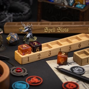 May include: Wooden dice trays and dice are displayed on a black surface. The trays are engraved with numbers and the words "Spell Slots." Several multi-sided dice are visible, along with miniature figurines and game tokens. The dice are various colors, including amber and purple.