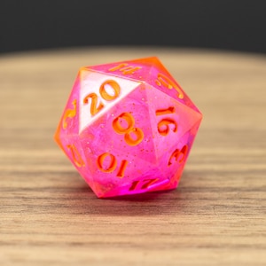 May include: A pink twenty-sided die with orange numbers. The die has a glittery finish.