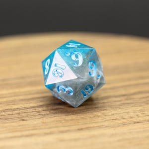 May include: A blue and white d20 dice with white numbers. The dice is made of resin and has a cloudy, translucent appearance.