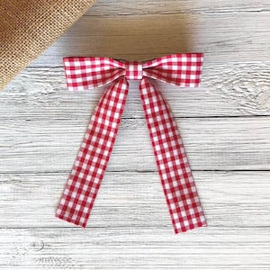 Puede incluir: Pajarita de cuadros rojos y blancos con colas largas. La pajarita está sobre una superficie de madera blanca.