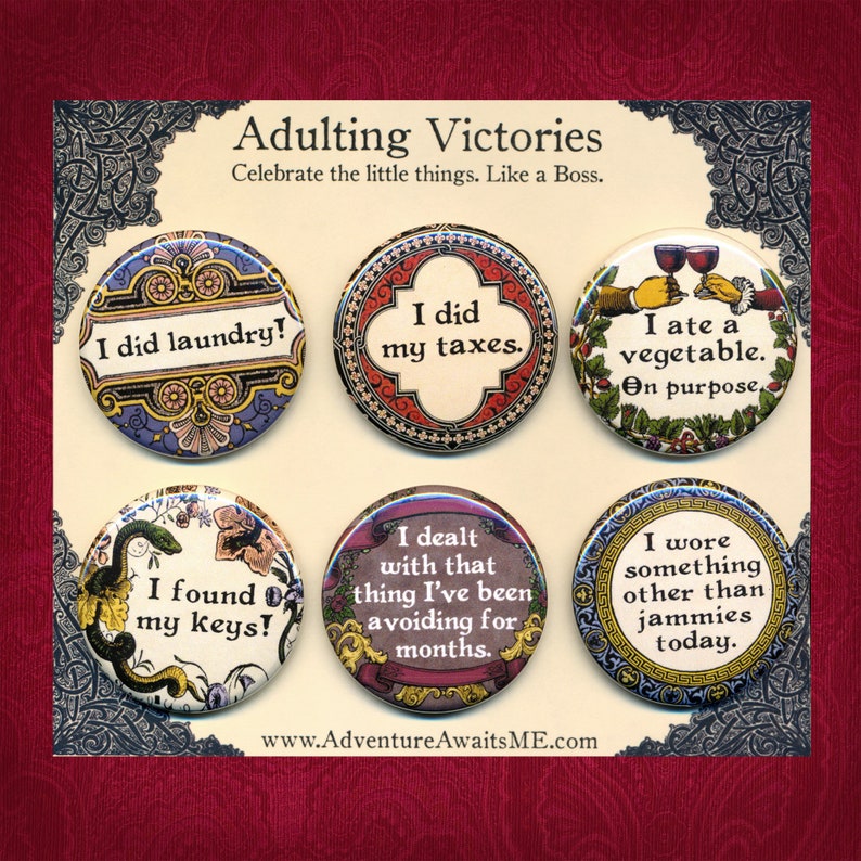 May include: Six round buttons with colorful designs and humorous sayings about adulting. The buttons feature sayings like "I did laundry!" and "I ate a vegetable. On purpose."
