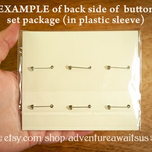 May include: A close-up of a white card with six silver button pins displayed on it. The card is in a clear plastic sleeve. The text "etsy.com/shop/adventureawaitsus" is printed on the bottom of the card.