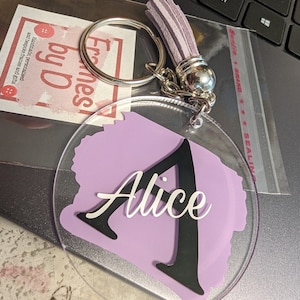 May include: A clear acrylic keychain with a purple background and the name "Alice" written in white and black lettering.