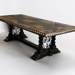 May include: A large, rectangular dining table with a dark wood top and intricate metal detailing. The table has a distressed finish and a decorative border around the edge.