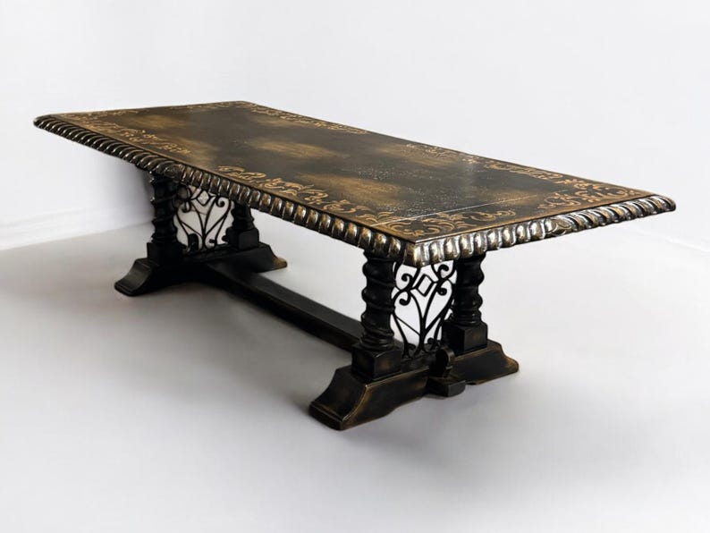 May include: A large, rectangular dining table with a dark wood top and intricate metal detailing. The table has a distressed finish and a decorative border around the edge.