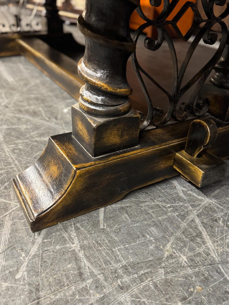 May include: Close-up of a dark wood table leg with a black and gold finish. The leg has a decorative scroll design and a square base.