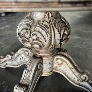May include: A distressed white and silver table base with a carved floral design and three legs.