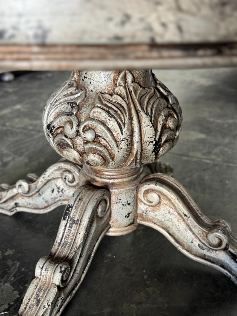 May include: A distressed white and silver table base with a carved floral design and three legs.