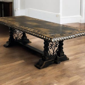May include: A long, black wooden table with ornate gold detailing and a scrolled edge. The table has a black metal base with intricate scrollwork.