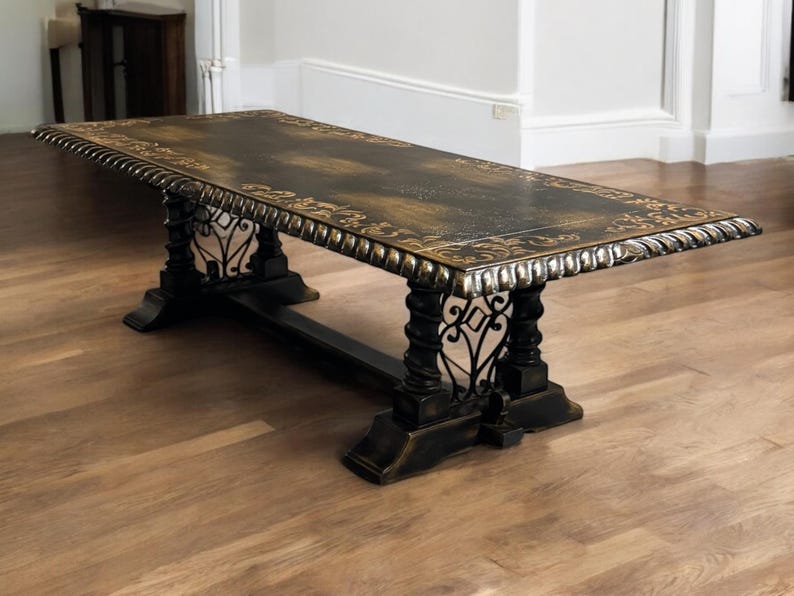 May include: A long, black wooden table with ornate gold detailing and a scrolled edge. The table has a black metal base with intricate scrollwork.