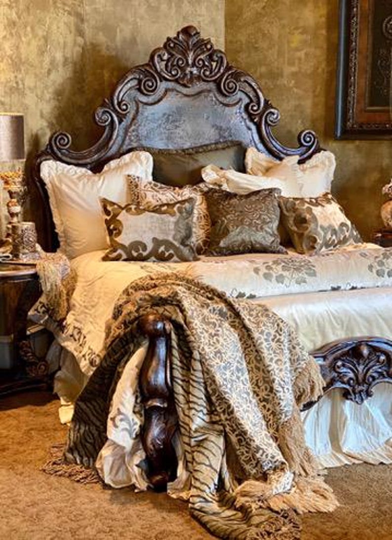 K&ouml;nnte beinhalten: Ein luxuri&ouml;ses Bett mit einem geschnitzten Kopfteil und aufwendigen Details. Das Bett ist mit Kissen und einer gemusterten Bettdecke geschm&uuml;ckt. Eine dekorative Decke mit Fransen ist &uuml;ber dem Fu&szlig;ende des Bettes drapiert. Die Farbpalette umfasst Gold, Braun und Creme.
