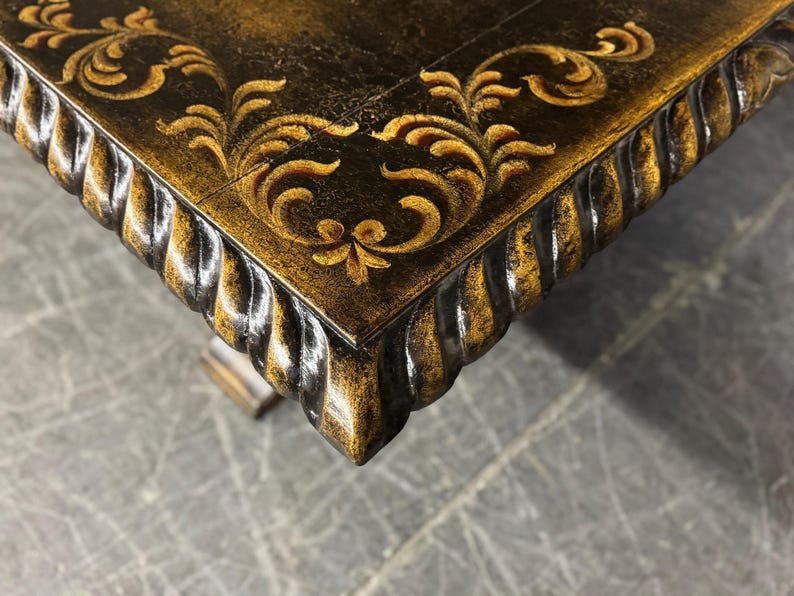 May include: Close-up of a dark brown table top with a gold leaf design. The table top has a rope-like edge.