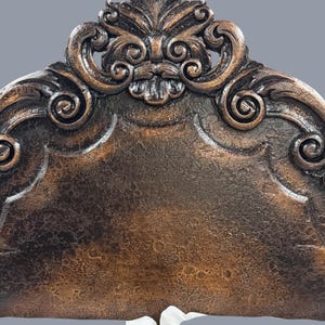 K&ouml;nnte beinhalten: Verziertes, dunkelbraunes Kopfende mit detaillierten Schnitzereien. Das Kopfende weist ein zentrales Blumendesign und verschn&ouml;rkelte Verzierungen auf. Die strukturierte Oberfl&auml;che hat ein antikes Aussehen. Das Kopfende ist Teil eines Bettrahmens.