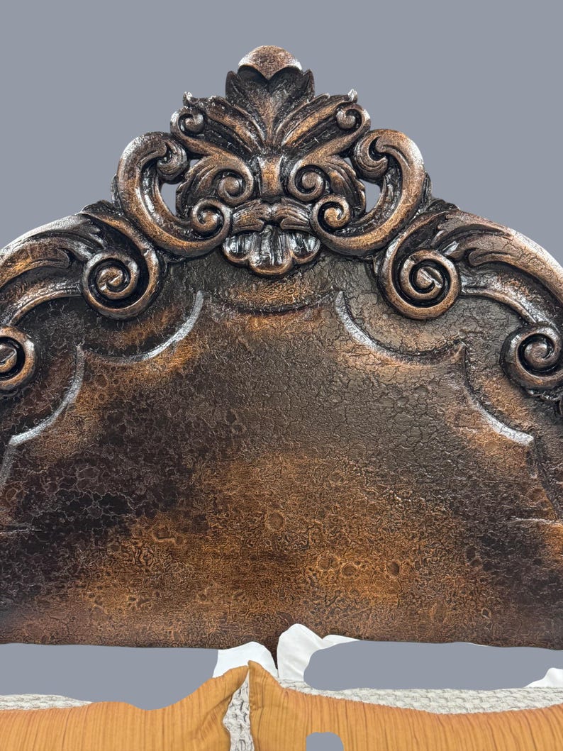 K&ouml;nnte beinhalten: Verziertes, dunkelbraunes Kopfende mit detaillierten Schnitzereien. Das Kopfende weist ein zentrales Blumendesign und verschn&ouml;rkelte Verzierungen auf. Die strukturierte Oberfl&auml;che hat ein antikes Aussehen. Das Kopfende ist Teil eines Bettrahmens.