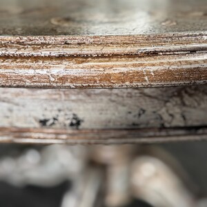 May include: Close-up of a distressed white and brown wooden table top with a decorative edge. The table has a pedestal base.