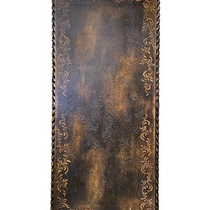 May include: A dark brown rectangular table top with a decorative border of rope and floral designs. The table top has a distressed, aged look.