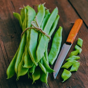 A bunch of fresh green beans and a knife are placed on a wooden surface.