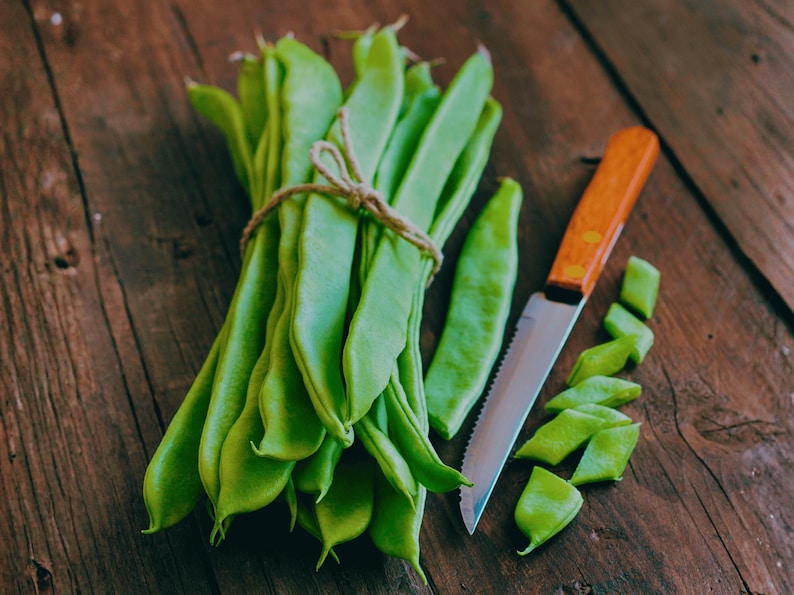 A bunch of fresh green beans and a knife are placed on a wooden surface.