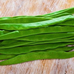 A pile of fresh green beans is neatly arranged on a wooden surface.